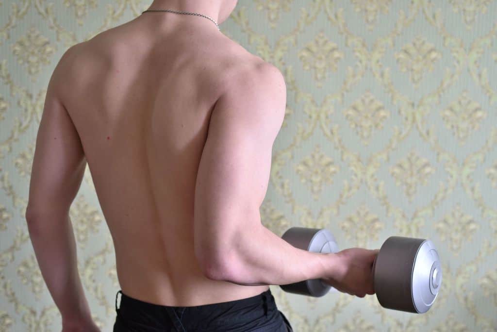 A guy using dumbbells to improve muscle mass - feature image