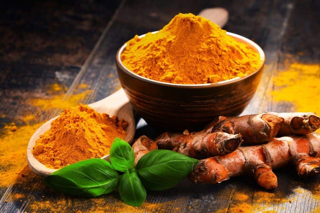 Composition with bowl of turmeric powder on wooden table - featured image